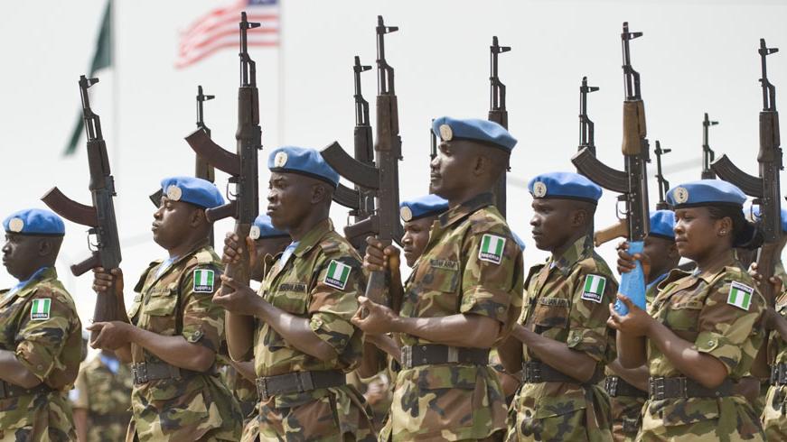 A group of Nigerian peacekeepers in uniform and wearing blue berets holding guns in a ceremonial salute.